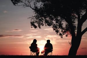 two people are sitting under a tree watching the sunset